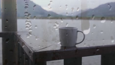 Animation-of-rain-drops-over-window,-cup-of-coffee-lake-and-landscape