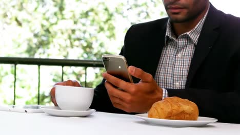 Animation-of-network-of-digital-icons-over-biracial-businessman-using-smartphone-at-a-cafe
