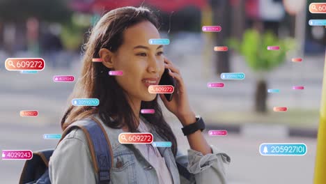 Animation-of-social-media-icons-against-happy-asian-woman-talking-on-smartphone-on-the-street