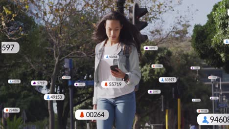 Animation-Von-Social-Media-Symbolen-Auf-Einer-Asiatischen-Frau-Mit-Trolley-Tasche,-Die-Mit-Ihrem-Smartphone-Die-Straße-überquert