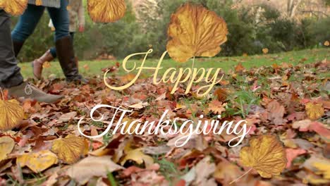 Animation-of-happy-thanksgiving-text,-autumn-leaves-against-low-section-of-people-walking-in-park