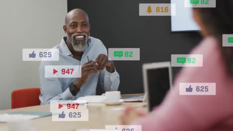 Anmation-of-social-media-icon-floating-over-african-american-man-discussing-with-a-woman-at-office