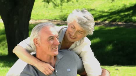 Senior-wife-hugging-her-husband-sitting-on-a-bench