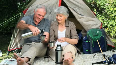 Aged-couple-drinking-coffee-sitting-near-a-tent