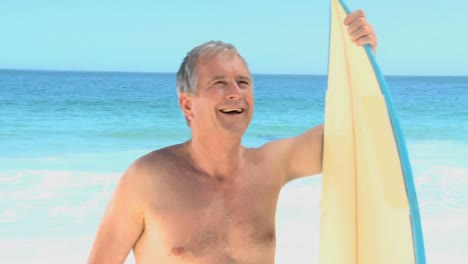 Elderly-man-looking-at-the-ocean-with-a-surfboard