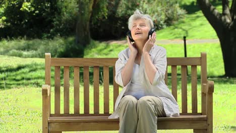 Elderly-female-listening-to-music-with-headset-on-a-bench