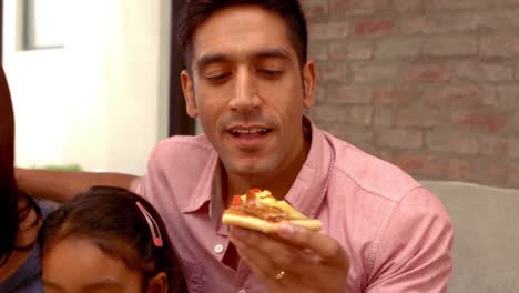 Smiling-Hispanic-family-eating-pizza-in-living-room