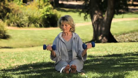 Old-woman-working-her-muscles-with-dumbbells-sitting-on-the-grass
