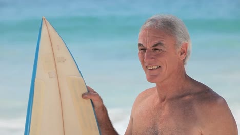 Aged-man-looking-at-the-ocean-with-a-surfboard