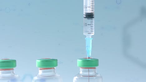Syringe-in-the-first-of-a-row-of-vaccine-vials-on-blue-background