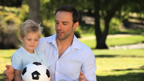 Vater-Und-Sohn-Spielen-Mit-Einem-Fußball,-Der-Auf-Dem-Rasen-Sitzt