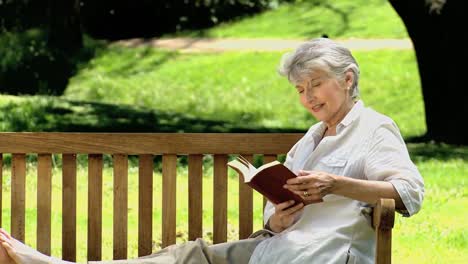 Senior-woman-reading-a-book-sitting-on-a-bench