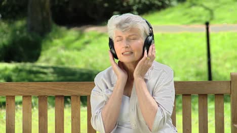 Ältere-Frau-Hört-Musik-Mit-Headset-Auf-Einer-Bank