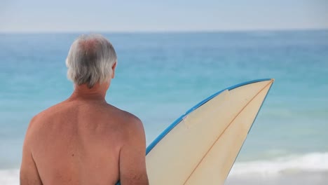 Älterer-Mann-Blickt-Mit-Einem-Surfbrett-Auf-Die-Wellen
