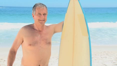Elderly-man-looking-at-the-beach-with-a-surfboard
