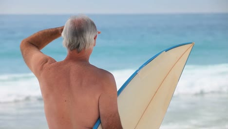 Alter-Mann,-Der-Mit-Einem-Surfbrett-Auf-Die-Wellen-Schaut