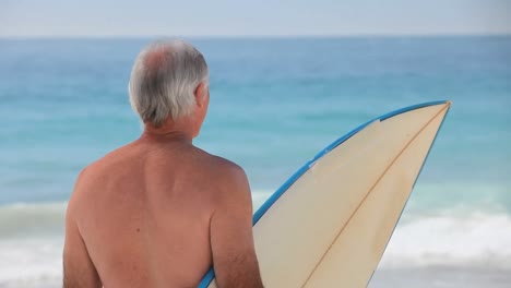 Mature-man-looking-at-the-ocean-with-a-surfboard
