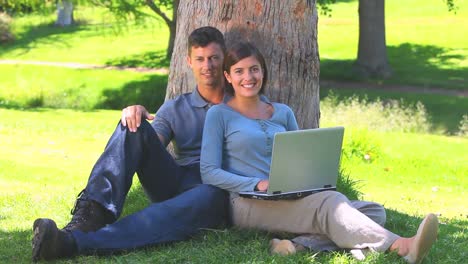 Young-couple-with-a-laptop-leaning-against-a-tree