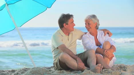 Elderly-couple-laughing-under-a-beach-umbrella