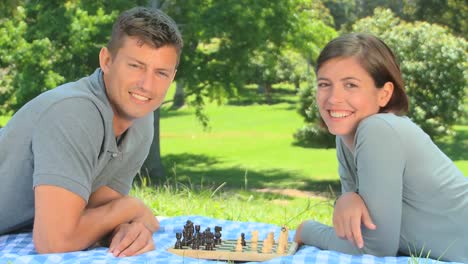 Young-couple-playing-chess-while-lying-on-the-grass