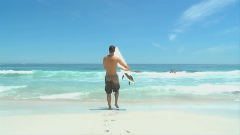 Hombre-Posando-Con-Tabla-De-Surf-Frente-Al-Mar