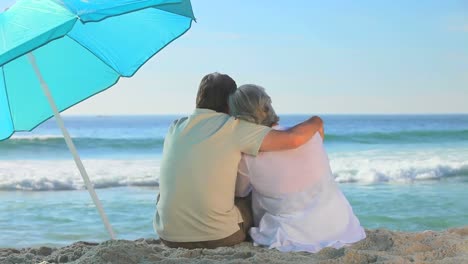 Älteres-Ehepaar-Mit-Blick-Auf-Das-Meer-In-Der-Nähe-Eines-Sonnenschirms