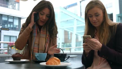 Pretty-friends-enjoying-coffee-in-cafe-using-phones