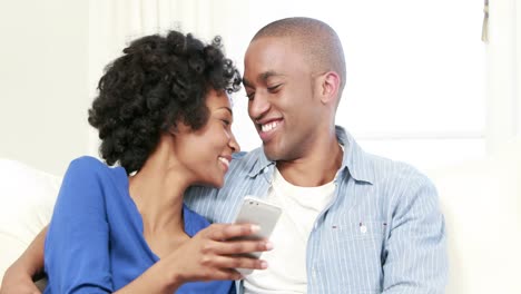 Glückliches-Junges-Paar,-Das-Auf-Der-Couch-Sitzt,-Während-Seine-Freundin-SMS-Schreibt