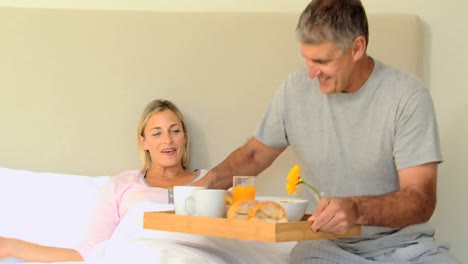 Young-woman-delighted-when-husband-brings-breakfast-in-bed