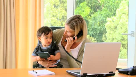 Young-mother-holding-baby-while-working-in-office