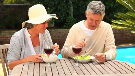 Mature-couple-laughing-over-lunch-by-a-swimming-pool