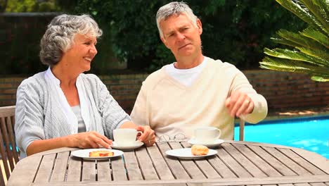 Retired-couple-having-coffee-by-the-swimming-pool