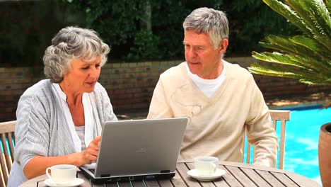 Mature-couple-sitting-outdoors-using-a-laptop