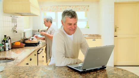 Mature-woman-cooking-while-husband-is-working-on-a-laptop