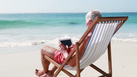 Retired-old-man-using-tablet-while-lying-on-deckchair