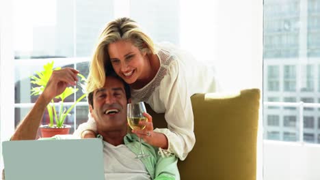 Young-couple-using-laptop-while-having-wine-in-living-room