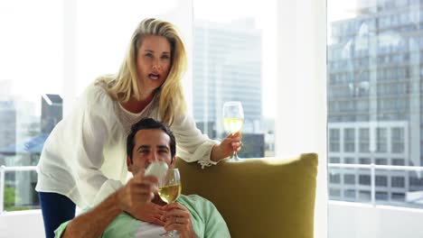 Young-couple-toasting-a-glasses-of-wine-while-watching-television-in-living-room