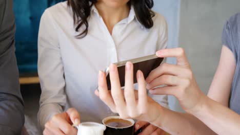 Women-showing-mobile-phone-to-businessman-while-having-coffee