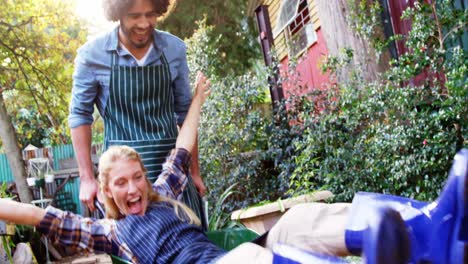Cheerful-man-giving-wheelbarrow-ride-to-female-gardener
