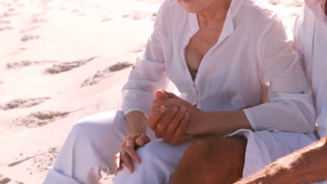 Senior-couple-sitting-and-holding-hands-on-the-beach