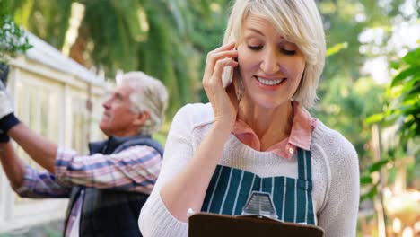 Mature-woman-talking-on-phone-while-man-checking-vegetables