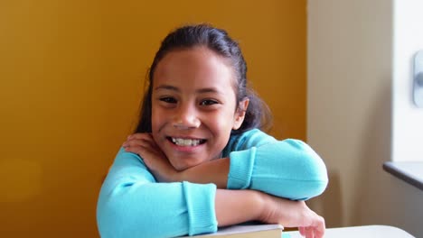 Porträt-Eines-Lächelnden-Mädchens,-Das-Sich-Im-Klassenzimmer-Auf-Einen-Stapel-Bücher-Stützt