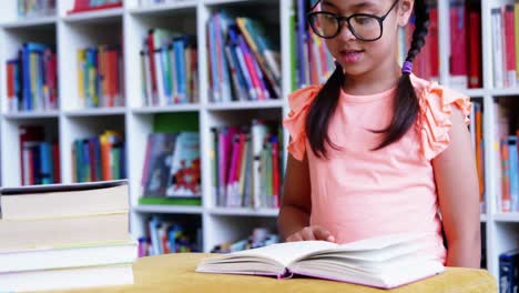 Schoolgirl-reading-book-in-library-at-school