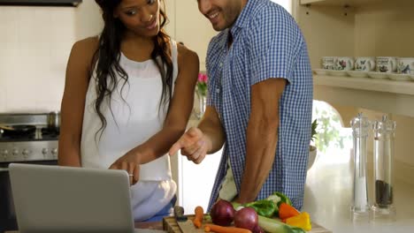 Young-couple-talking-while-using-laptop-in-kitchen