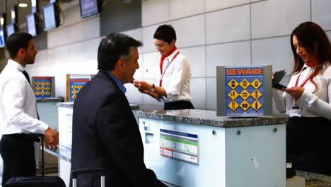 Zwei-Weibliche-Flughafenmitarbeiter-Kontrollieren-Ihren-Reisepass-Und-Interagieren-Mit-Einem-Pendler-Am-Check-in-Schalter