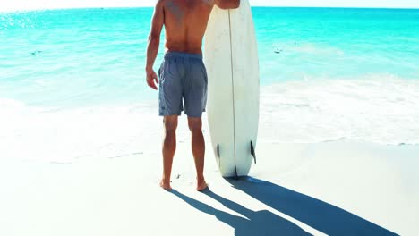 Man-standing-on-beach-with-surfboard