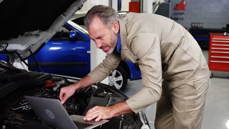 Mechanic-using-laptop-while-servicing-a-car-engine