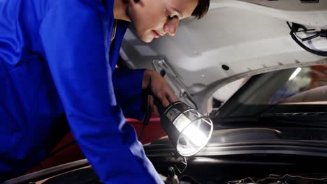 Female-mechanic-examining-car-engine-using-flashlight
