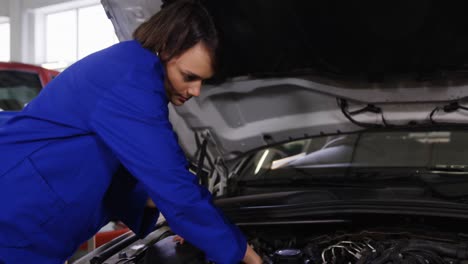Female-mechanic-talking-on-a-mobile-phone-while-servicing-a-car