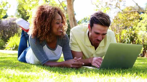 Couple-lying-on-grass-and-using-laptop-in-park